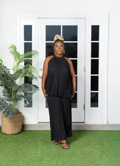 Woman in a black pleated outfit with a neck closure standing in front of a white door.