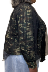 A person shown from the side wearing a sheer black long-sleeve top with a green, brown, and beige camouflage pattern, paired with light blue jeans against a white background.