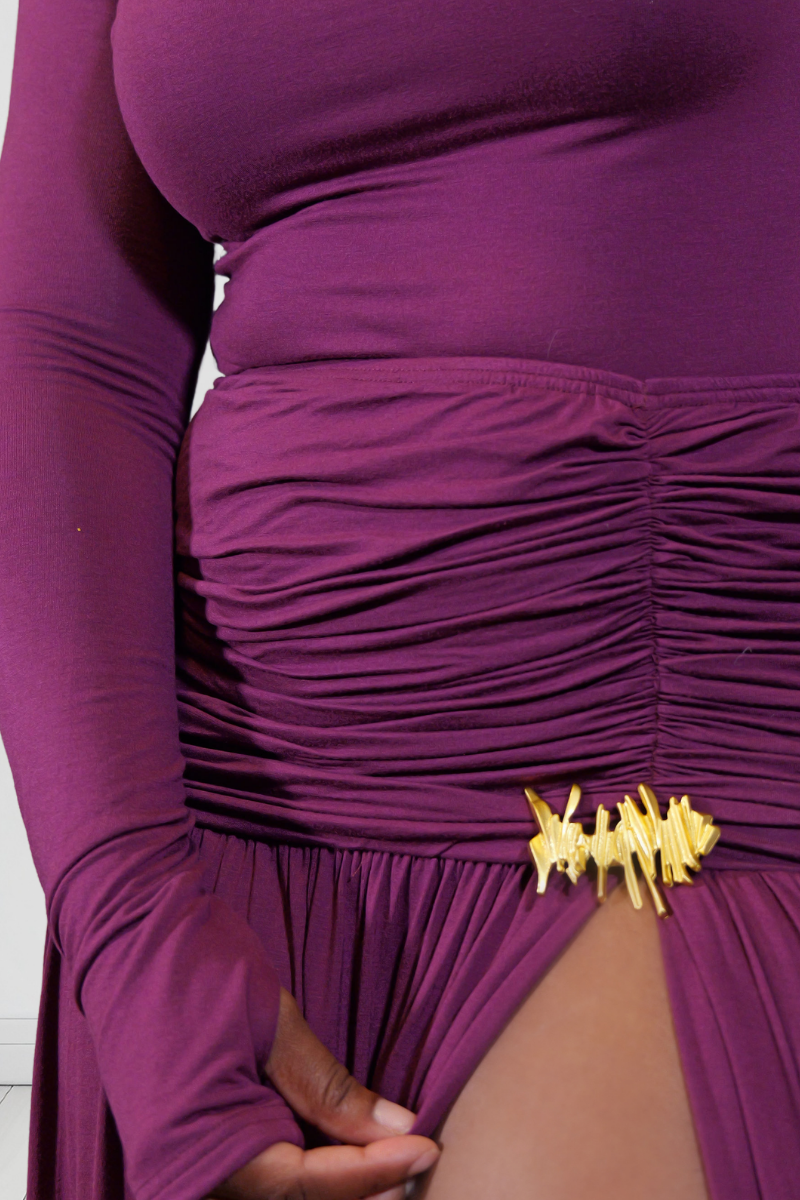 A close-up of a person wearing a ruched long-sleeve dress in deep purple with a gold abstract brooch.