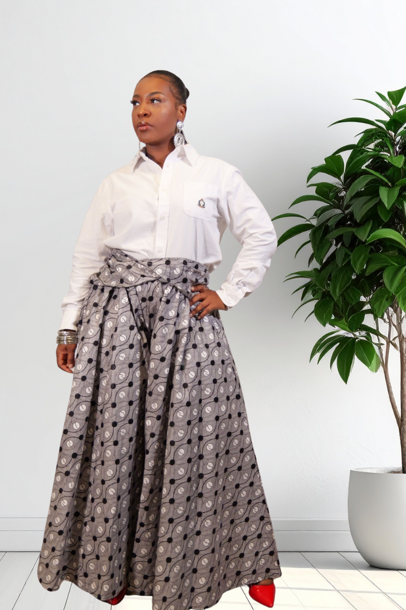 A woman modeling a white long-sleeve button-up shirt paired with high-waisted, full-length wide leg pants, standing next to a potted green plant.
